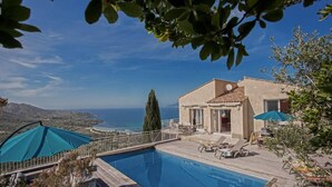 Ein Pool mit Meerblick, ein Haus mit Balkon und Gartenmöbeln.