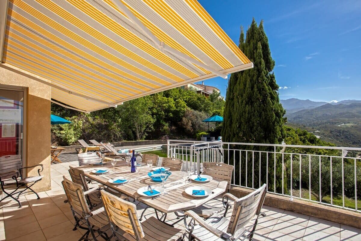 An outdoor dining area with a table set for four, surrounded by chairs, under a striped awning.