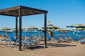 Ein Strand mit blauen Liegestühlen und bunten Sonnenschirmen.