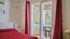 A bedroom with a bed, a sliding glass door to a balcony, and a small table with a chair.