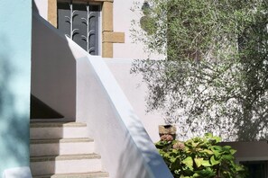 A white building with a staircase leading to a window with a metal gate.