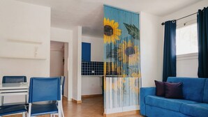 En stue med en blå sofa, et spisebord med stole og et køkken i baggrunden.