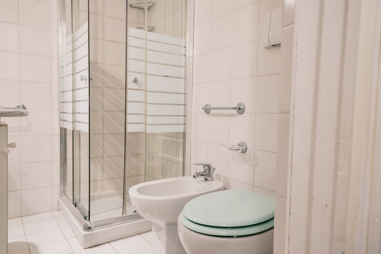 Une salle de bain dotée d’une douche à parois de verre, d’un bidet et de toilettes avec un abattant vert.