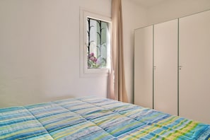 A bedroom with a bed, a window with curtains, and a wardrobe.