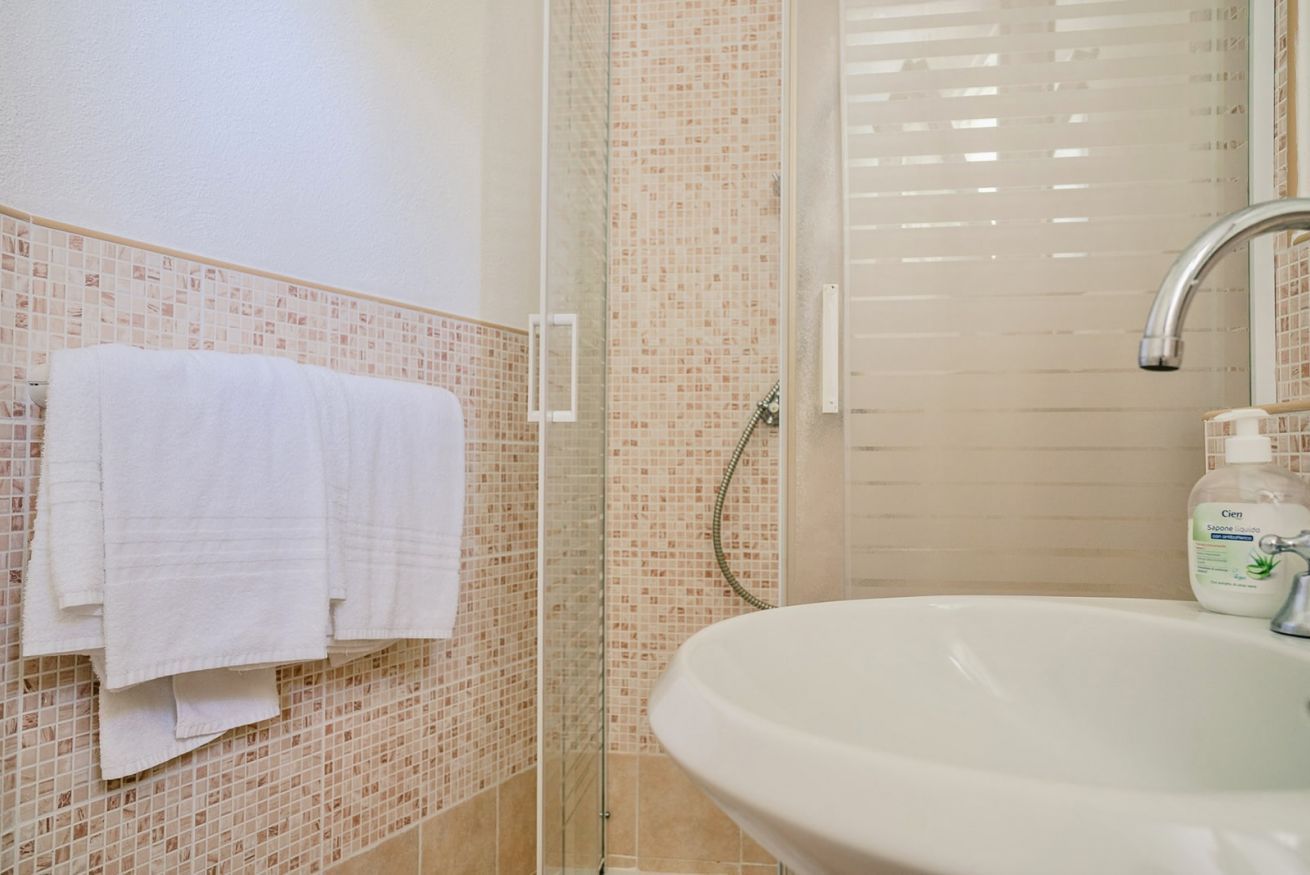 A bathroom with a tiled shower, a sink, and a towel rack.
