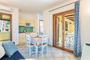 Un espacio habitable compacto con zona de comedor, kitchenette y puerta corrediza de vidrio que da a un patio exterior.