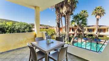 Un balcón con mobiliario de mimbre, piscina y palmeras.