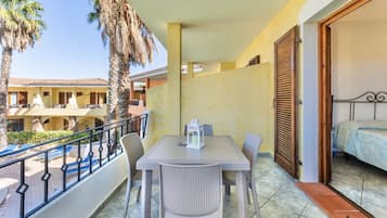 Un balcón con mesa y sillas, vistas a una piscina, y un edificio con balcones al fondo.