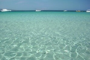 Une mer turquoise aux eaux limpides, avec des bateaux qui se dessinent à l’horizon.