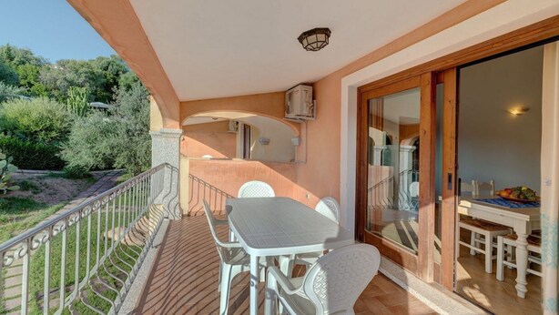 A balcony with a table and chairs, a glass door leading to a dining area, and a view of the surrounding greenery. - Badus Two-room apartment, WIFI, A.C, swimming pool (Badesi)