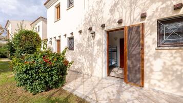 Un edificio bianco con un ingresso piastrellato, una porta in legno e un piccolo giardino con fiori rossi.