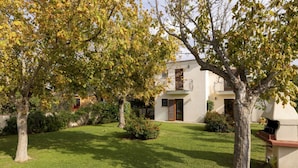 A well-maintained garden with a white building featuring a balcony and a barbecue area.