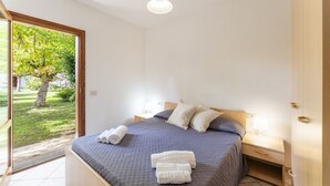 A bedroom with a bed, a nightstand, a lamp, and a view of a garden through a glass door.