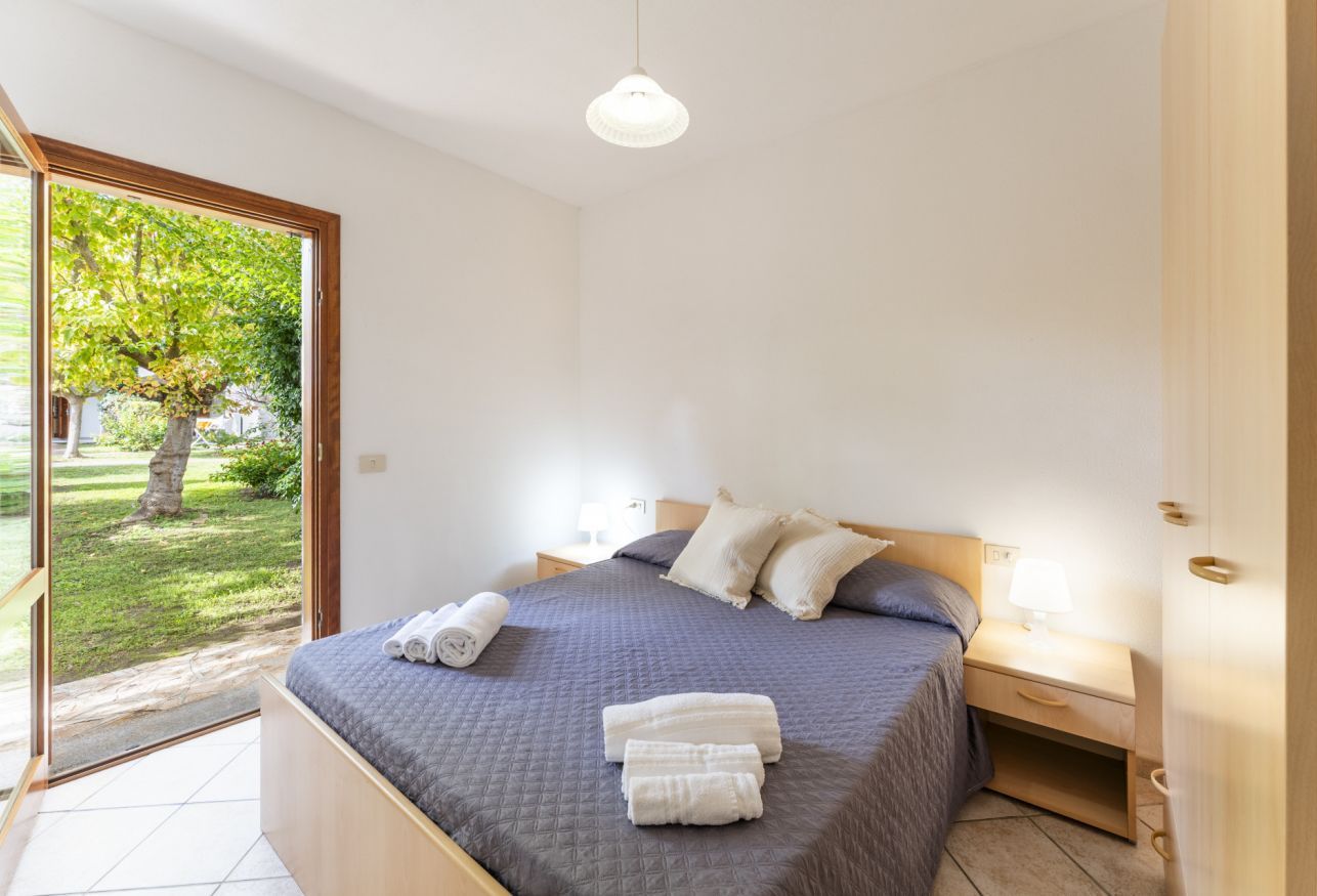 Una camera da letto con un letto, un comodino, una lampada e vista su un giardino tramite una porta in vetro.
