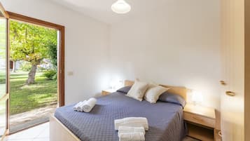 Una camera da letto con un letto, un comodino, una lampada e vista su un giardino tramite una porta in vetro.