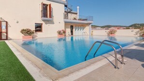 A swimming pool with a metal ladder, surrounded by a building with a balcony and potted plants.