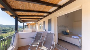 A balcony with two lounge chairs, a sofa, and a bed in a room with a view of the landscape. - Three-room apartment with 6 beds, sea view, about 65/70 sq m, living room with kitchenette, double or twin sofa bed, double bedroom, one twin bedded room or with bunk bed, bathroom. Side or front sea view. <br>Apartments arranged on different levels. Spa (Baja Sardinia)