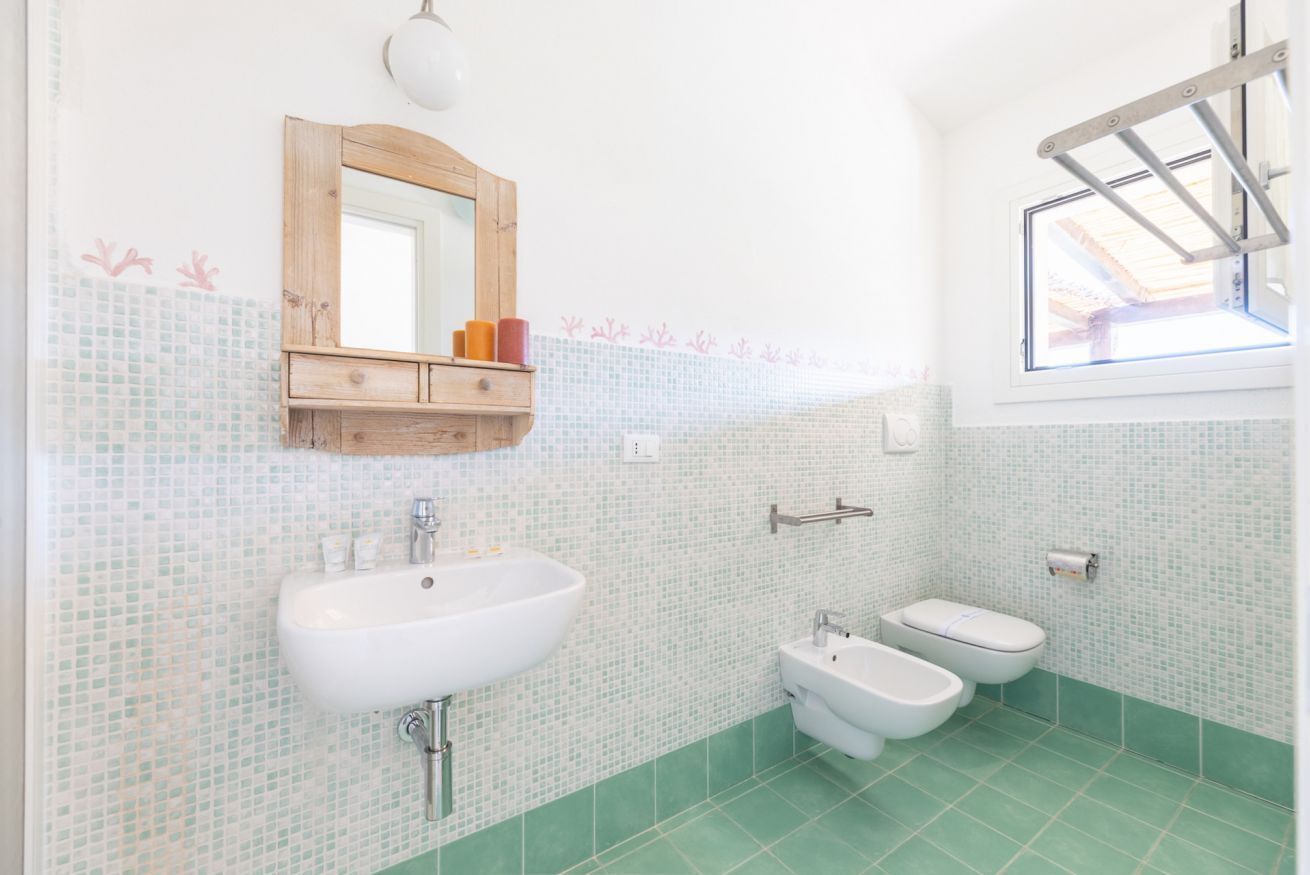 Ein Badezimmer mit einem weißen Waschbecken, zwei Toiletten, einem Spiegel und einem Fenster.