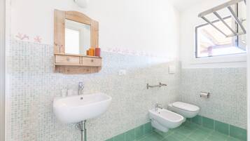 Ein Badezimmer mit einem weißen Waschbecken, zwei Toiletten, einem Spiegel und einem Fenster.