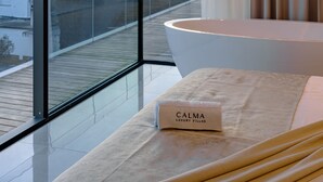 A modern bathroom with a large bathtub, a glass-enclosed balcony, and a view of the sunset over the water.