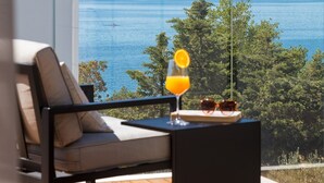 A balcony with a view of a lake, a chair, a table with a glass of orange juice, and sunglasses.