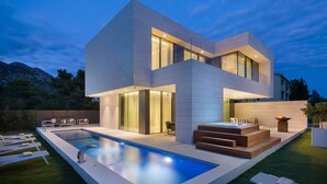 A modern two-story house with a swimming pool, outdoor seating, and a fire pit.