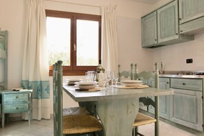 A dining area with a table set for four, a window with curtains, and light-colored wooden cabinets.
