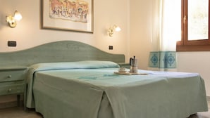 A room with a bed, a nightstand, a framed picture on the wall, and a window with curtains. - Two-room apartment with 4 beds, about 38 sq m, living room with kitchenette, sofa bed or bunk bed, bedroom with double bed (separable beds), bathroom with shower. Possibility 1 infant in cot. <br>The apartments are arranged over three floors (ground, fir (Sos Alinos)