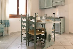A dining area with a table set for two, wooden chairs with woven seats, a candle, and a bottle of wine.