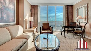 Una habitación de hotel moderna con un ventanal grande, una mesa redonda de vidrio, un sofá, una silla y una lámpara.