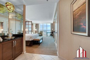 A hotel room with a large bed, a desk, a chair, a window with a view, and a kitchen area with cabinets and a countertop. - Jacuzzi & Kitchenette Studio at MGM The Signature (Las Vegas)