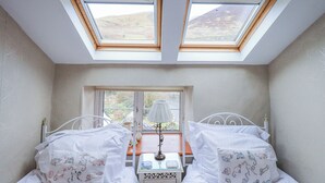 Ein Schlafzimmer mit zwei Betten, einem Oberlicht, einem Fenster und einem Nachttisch mit einer Lampe.