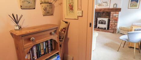 A cozy room with a wooden bookshelf filled with books and board games, a small table with a candle, and a door leading to a living area with a fireplace.