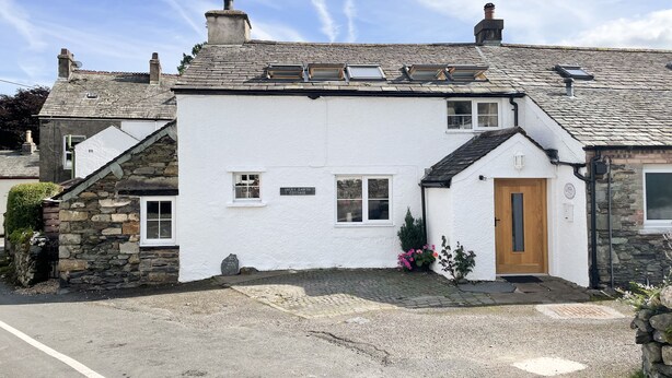 Ein weißes Cottage mit einer Stein-Fassade, einer Holztür und einer Schotterauffahrt.