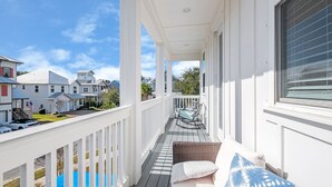 A covered porch with a white railing, a wicker sofa, and a view of neighboring houses. - Amazing Beach house Steps from 30a | Golf Cart | Beach, Pool & Lake access! (Inlet Beach)