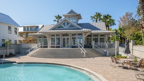 A pool area with a building featuring a large windowed entrance, a covered patio, and a staircase leading to a deck. - Amazing Beach house Steps from 30a | Golf Cart | Beach, Pool & Lake access! (Inlet Beach)