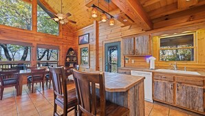 Een houten chalet van binnen met een eethoek, keuken en grote ramen.