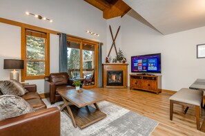 A spacious living room with a fireplace, wooden flooring, leather furniture, and a television displaying a streaming service.