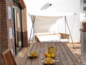 Une table en bois avec des tasses jaunes et un pichet, une chaise en osier et un auvent blanc.