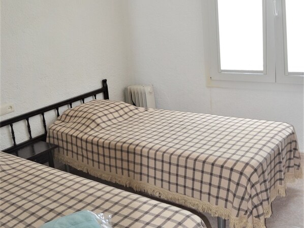 A small, simple room with two beds, plain walls, and a window.