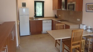 Cozinha compacta com armários de madeira, máquina de lavar louça embutida e um pequeno espaço de jantar com mesa e cadeiras.