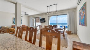A spacious living area with a large dining table, wooden chairs, and a TV mounted on the wall. - Steps to Sand- Serene Beachfront Getaway in Isla Mujeres, Mexico. (Isla Mujeres)