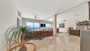 A spacious living area with a large window overlooking the ocean, a wooden bench, and a kitchen area with a refrigerator. - Steps to Sand- Serene Beachfront Getaway in Isla Mujeres, Mexico. (Isla Mujeres)