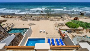 A pool with blue lounge chairs, a sandy beach, and a view of the ocean. - Steps to Sand- Serene Beachfront Getaway in Isla Mujeres, Mexico. (Isla Mujeres)