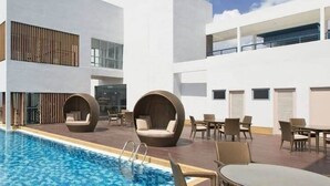 Un área de piscina en la azotea con una piscina azul cristalina, sillones de descanso y mesas.