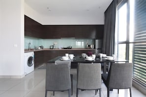 Une cuisine moderne avec un coin repas, un lave-linge et une grande fenêtre équipée de stores.