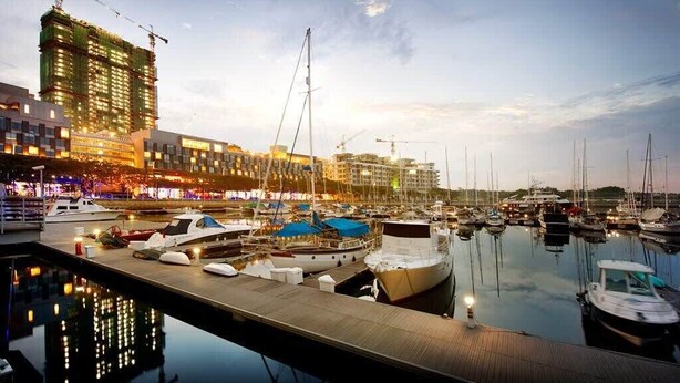 Un puerto deportivo con barcos amarrados, una grúa de construcción y edificios al fondo.