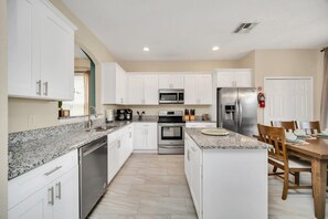 A modern kitchen with white cabinets, granite countertops, stainless steel appliances, and a dining area with wooden chairs.