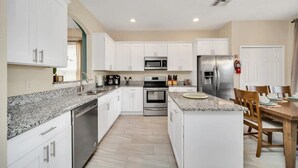 A modern kitchen with white cabinets, granite countertops, stainless steel appliances, and a dining area with wooden chairs. - Southwest facing pool! 5 Miles from Disney. (Kissimmee)