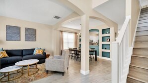 A spacious living area with a sofa, armchair, and coffee table, a staircase, and a dining area with chairs and a table. - Southwest facing pool! 5 Miles from Disney. (Kissimmee)